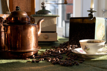coffee grinder, coffee beans, a coffee pot and an old-fashioned coffee cup on a table with a green...