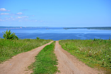 Fototapeta na wymiar country road with green grass going to horizon with Volga river and clear blue sky on background