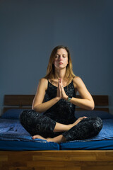 Beauty young caucasian woman sitting in yoga position on bed. Relaxing routine before or after sleeping