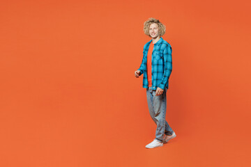 Full body sideways smiling fun young blond caucasian man wear blue shirt orange t-shirt look camera walking going strolling isolated on plain red background studio portrait. People lifestyle concept.