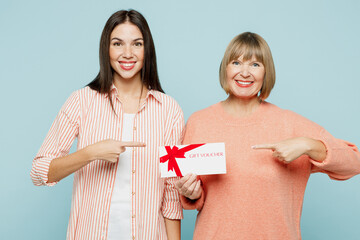 Elder parent mom with young adult daughter two women together wear casual clothes hold point finger on store gift certificate coupon voucher card isolated on plain blue background. Family day concept.