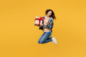 Full body side view young smiling happy woman wear blue shirt beige t-shirt present box with gift ribbon bow look aside isolated on plain yellow background studio portrait. People lifestyle concept.