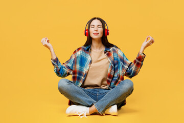 Full body young woman wearing blue shirt beige t-shirt headphones hold spreading hands in yoga om aum gesture relax meditate try to calm down listen music isolated on plain yellow background studio.