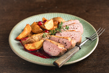 Roasted duck breast with potatoes and berry sauce on wooden background, selective focus