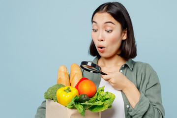 Young surprised woman in casual clothes hold brown paper bag with food products look through...