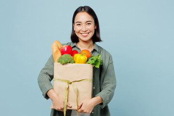 Young fun woman wear casual clothes hold brown paper bag with food products with measure tape on packet isolated on plain blue cyan background studio portrait Delivery service from shop or restaurant