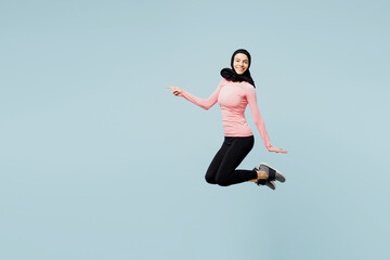 Fototapeta na wymiar Full body young asian muslim fitness trainer sporty woman wears pink abaya hijab spend time in home gym jump high point aside isolated on plain blue background studio. Workout sport fit abs concept.