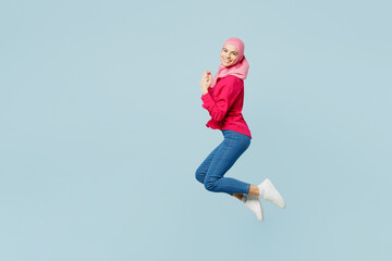 Fototapeta na wymiar Full body side view fun young arabian asian muslim woman wear pink abaya hijab jump high do winner gesture isolated on plain pastel light blue cyan background studio portrait People uae islam concept.