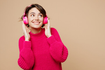 Young cheerful joyful smiling caucasian woman wear pink sweater headphones listen to music look...