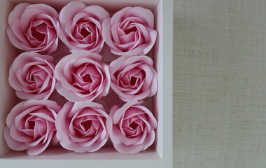 9 artificial pink roses arranged in a white cardboard box on a cream background. Pink Valentine's Day roses represent the sweetest love. Pink flower boxes packed in a box to be given as a gift.
