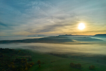 Aerial view of fog landscape at sunrise. Hill range behind agricultural fields in autumn. Blue sky for copy space. Germany, Nurtingen, Tiefenbachtal.