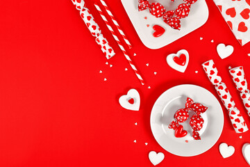 Valentine's Day decoration with candy, heart ornaments and sugar sprinkles on red background with copy space