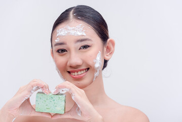Beautiful Asian lady holding a bar of facial soap while forming a heart hand sign. Beauty products...