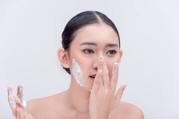 A studio photo of an Asian girl washing the tip of her nose with a foamy facial soap. Plain white background