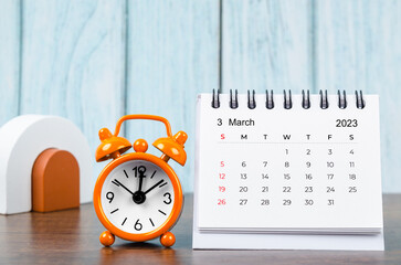 A March 2023 Monthly desk calendar for the organizer to plan 2023 year with alarm clock on wooden table.