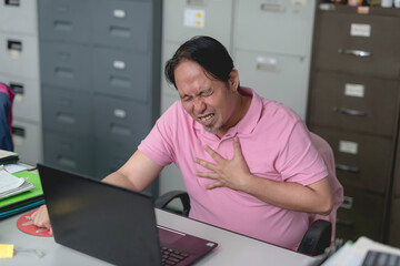 A mans feels chest pain, possibly angina or severe heartburn, while working at his desk in the office. - obrazy, fototapety, plakaty