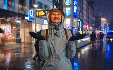 Fototapeta na wymiar snowfall woman in a blue jacket and yellow hat christmas outside, city portrait in snowfall, young model posing in Dusseldorf city, fabulous advent evening