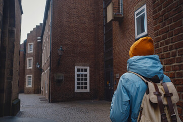 Fototapeta na wymiar winter travel to Dusseldorf, Germany. young Asian tourist in blue jacket and yellow hat (symbol of Ukraine) walks through sights of old town or Altstadt. Popular center of Rheinland and Westphalia