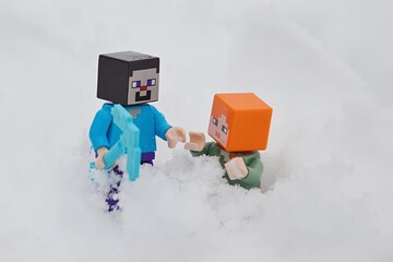 Fototapeta premium LEGO Minecraft figure of Steve with diamond pickaxe helping Alex out of deep snow after avalanche. 