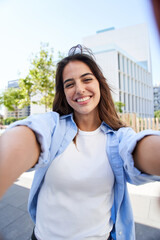 Vertical selfie of a Young beautiful woman smiling at university campus. Trendy girl in casual attire. Positive cheerful female student posing outdoors for sharing in social media app. Caucasian lady