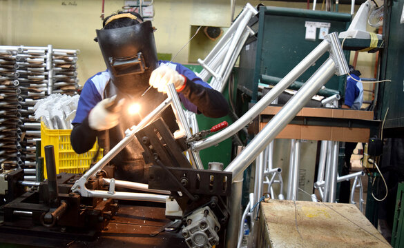 Industrial worker doing welding of a bicycle manufacturing industry. Workers wear work safety uniforms and wear anti-radiation helmets