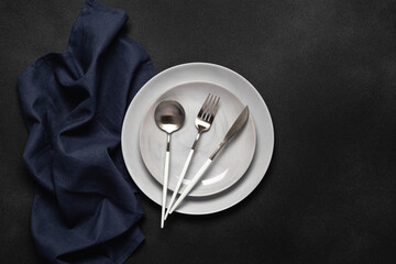 Gray plates and silver flatware on a dark black grunge background. Top view. Card or menu template, flat design. Tableware, crockery. Aerial view, copy space. Table setting. Flat design.