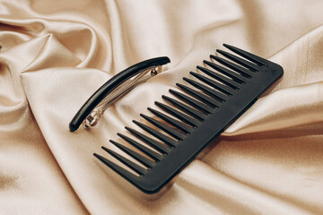 Elegant black hair clip and comb on a silk golden background. - obrazy, fototapety, plakaty