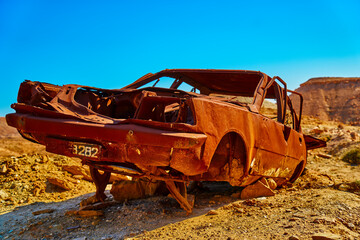 Completely rusted wrecked car in the desert hills of Tunisia under a blue sky