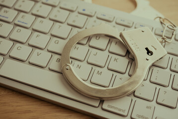 Close up police handcuffs on white keyboard background. Cybercrime, online internet financial scam, internet fraud, phishing email hacker, swindler concept.
