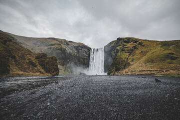 Iceland landscape with waterfall in the background and black colored earth with grayish sky