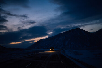 Fototapeta na wymiar Highway in iceland with car coming from the front with headlights on and with snowy mountain in the background at dusk