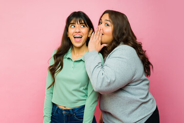 Women best friends sharing secrets looking surprised