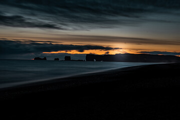 Iceland landscape at sunset on black sand beach with silk effect water and mountains with special shapes in the background