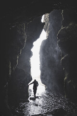 Person entering a waterfall grotto in iceland silhouetted against a background illuminated by natural light