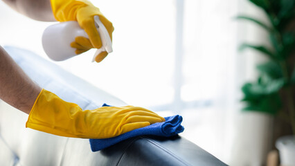 Person cleaning the room, cleaning staff is using cloth and spraying disinfectant to wipe the sofas...