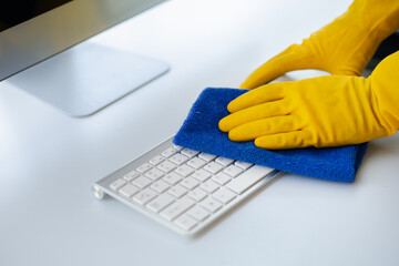 Person cleaning room, cleaning worker is using cloth to wipe computer keyboard in company office...