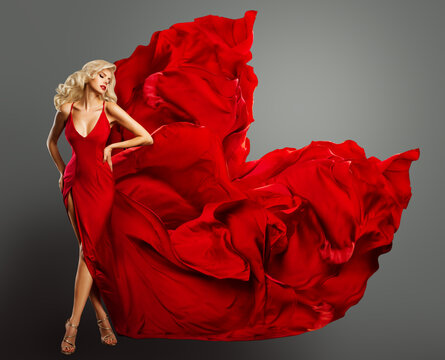 Fashion Model in Red Dress as Heart Shape. Glamour Blond Woman in Evening Silk Gown flying on Wind. Sexy Girl dancing in Fantasy Dress over Gray Background