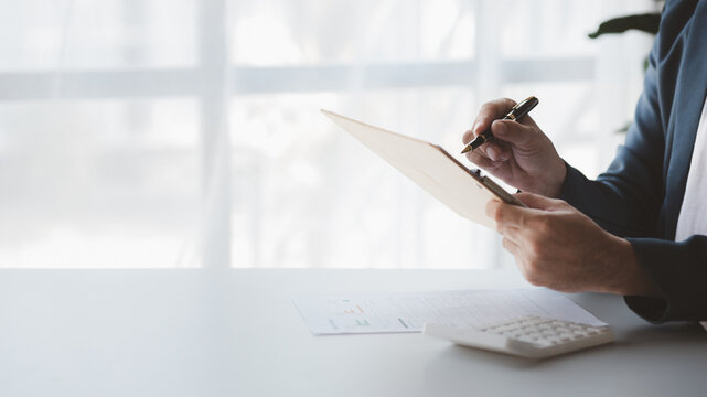 A close-up view of a businessman pointing at a bar chart on a company financial document prepared by the Finance Department for a meeting with business partners. Financial concept.