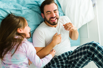 Young daughter in pajamas tickling her dad