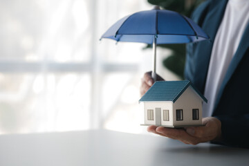 Individuals holding small umbrellas and model homes, housing insurance against impending loss and...