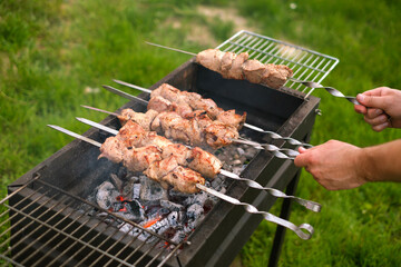 Juicy pieces of pork on a spit are fried on coals. A man is preparing a barbecue in the yard
