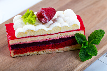 A piece of raspberry sponge cake with fluffy cream and mint on a wooden board. Close up