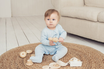 little cute baby in blue overalls plays with wooden toys sitting on a wicker carpet at home, environmentally friendly toys and the concept of motherhood and environmental care