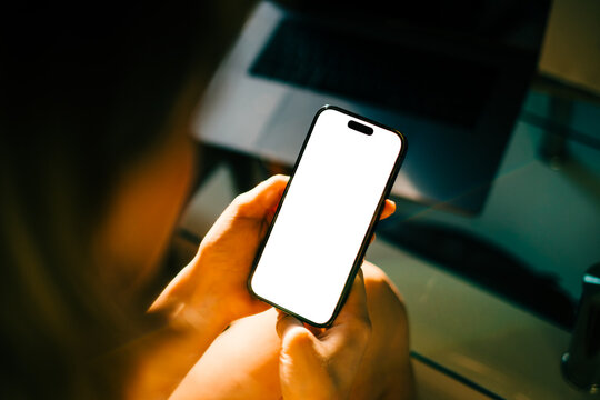 Woman holding mobile phone with white screen mock up, resting on a sofa in living room at home.	