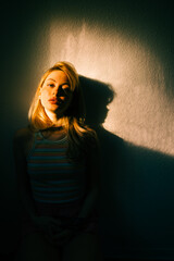 Portrait of attractive caucasian woman with blonde hair posing in sunset light indoor.