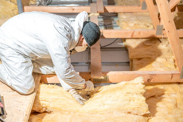 man insulates the roof and ceiling of the house with glass wool