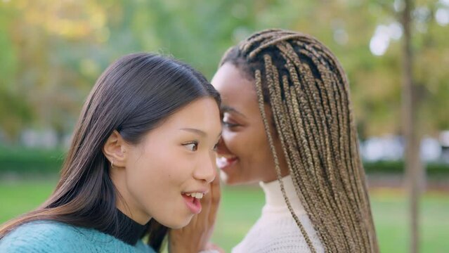 African woman tells friend a secret in her ear outdoors
