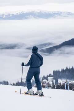 A Snowboarder In A Red Jacket Stands On Top Of A Mountain And Looks Into The Distance