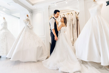 Naklejka premium Portrait of smiling cheerful happy love asian couple fashion bride man and woman posing in white wedding dress for pre wedding hug together at wedding interior fashion studio