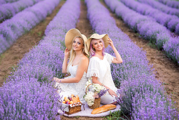 Two friends, young women in big hats are sitting in lavender flowers. Picnic on the field